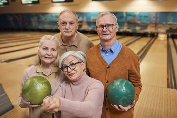 Waist up portrait of group of senior people taking selfie photos while playing bowling and enjoying active entertainment at bowling alley
