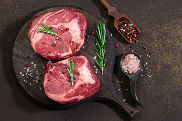 Raw organic beef steaks with spices and herbs  on dark rustic background. Healthy food concept.