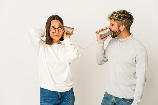 Young hispanic friends talking through a tin can system touching back of head, thinking and making a choice.