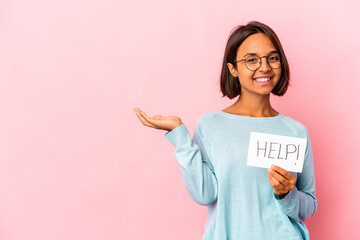 Fototapeta na wymiar Young hispanic mixed race woman holding a help poster showing a copy space on a palm and holding another hand on waist.