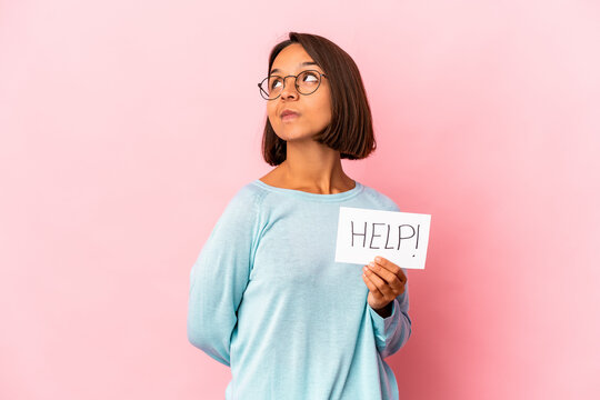 Young hispanic mixed race woman holding a help poster dreaming of achieving goals and purposes