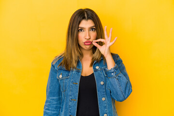 Young indian woman isolated on yellow background with fingers on lips keeping a secret.