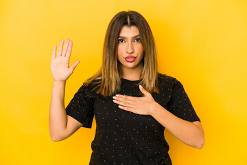 Young indian woman isolated on yellow background taking an oath, putting hand on chest.