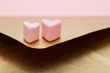Golden paper craft envelope with two hearts from marshmallow isolated on pink background