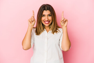 Young indian woman isolated on pink background indicates with both fore fingers up showing a blank...