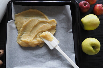 Top view of making roll-up pastila,homemade fruit leather . Fruit puree on a black baking sheet with a white spatula on a wooden table. The concept of making natural sweets from apples and bananas