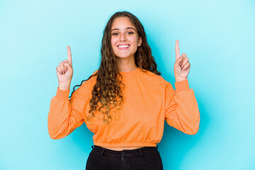 Young caucasian curly hair woman isolated indicates with both fore fingers up showing a blank space.