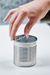 Hand holding a tin with boiled green peas on a white table
