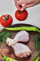 Woman hand holding juicy tomato on top of raw chicken legs plate