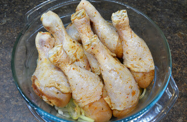 raw, marinated chicken drumsticks stacked in a glass baking dish, close-up photo