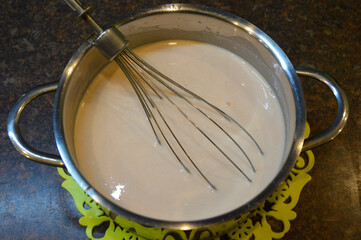 sour cream tomato sauce is poured into a stainless steel pan, inside there is a whisk for whipping