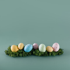 Easter colored eggs in a row laying on the moss on the green background. Happy Easter holiday. Muted colors. Square card. Selective focus. Copy space.