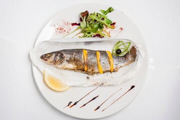 Fried fish with lemon on white plate. Dandelion salad.