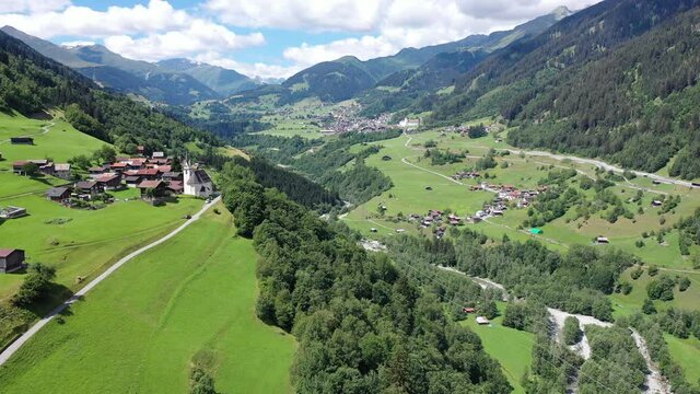 Picturesque aerial view of houses of small Swiss village Cavardiras in mountain valley in sunny summer day. High quality 4k footage