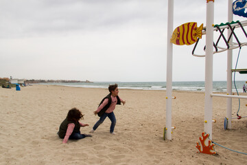 Obraz premium children playing on the beach, winter day, next to the swings