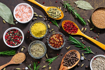 Assortment of organic aromatic spices and herbs on dark brown stone background top view. Healthy food ingredients concept.