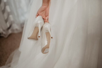bride holds a pair of white shoes. A pair of bridesmaid shoes.