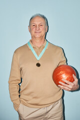 Vertical waist up portrait of smiling senior man holding bowling ball while standing against blue...