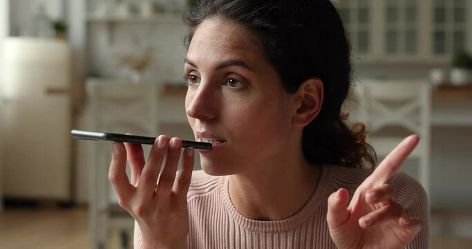 Close up head shot happy millennial caucasian woman recording audio message, responding in social networks to family or friends, activating voice assistant or using voicemail application on smartphone