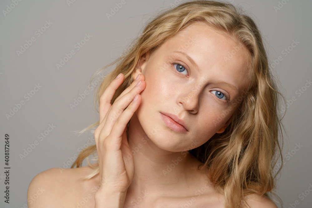 Wall mural closeup of pretty young woman face with blue eyes, curly natural blonde hair, has no makeup, touchin