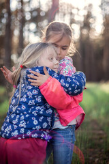 Cute girl hugging her small sister with love and tenderness during their walking in the forest at autumn, national hug and friendship day, casual lifestyle, outdoor