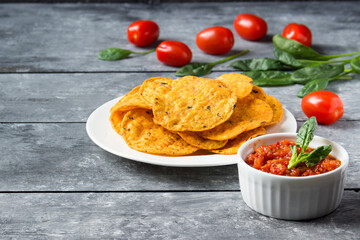 Tomato salsa and crispy potato chips on a plate.
