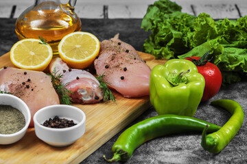Raw chicken fillet and legs on wooden plate with fresh vegetables, spices and glass of oil