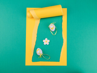 easter card with eggs and flowers.

Easter eggs with a flower in a yellow torn paper frame on a green background, top view close-up.