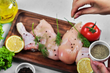 Hand adds spices to wooden plate of raw chicken meats on white background