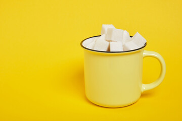 cubes of white sugar in a yellow cup on a yellow background