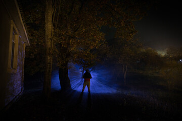 strange light in a dark forest at night. Silhouette of person standing in the dark forest with light. Horror halloween concept. strange silhouette in a dark spooky forest at night