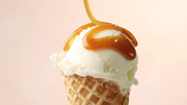 melted caramel sauce flowing on vanilla ice cream scoop in waffle cone close up on beige background. perfect summer dessert