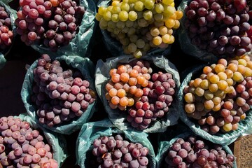 Bundle of white and red/purple/black grapes all placed at a market with vivid colors and healthy appearance. The fruits are tasty, full of vitamins and good for diet.
