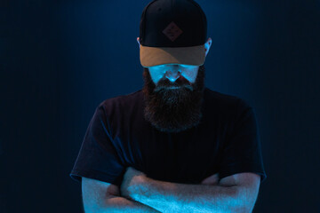 man with beard and baseball cap with dark and blue background unrecognizable face 