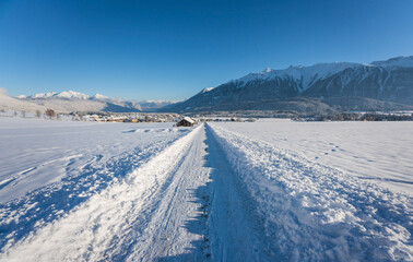 Snow covered walking path through alpine winter landscape to the village of Wildermieming, Tirol, Austria