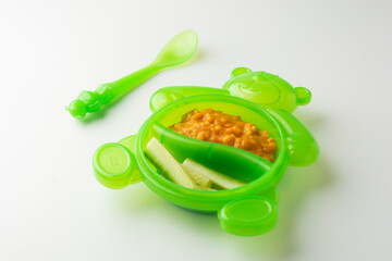 Baby food in green plastic bowl. First food for baby. Mashed vegetables with fresh cucumber slices.