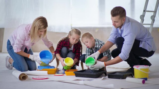 finishing work, joyful parents with girl and disabled boy pour colored paints from buckets into a pallet for painting walls in house, renovation and renovating an apartment