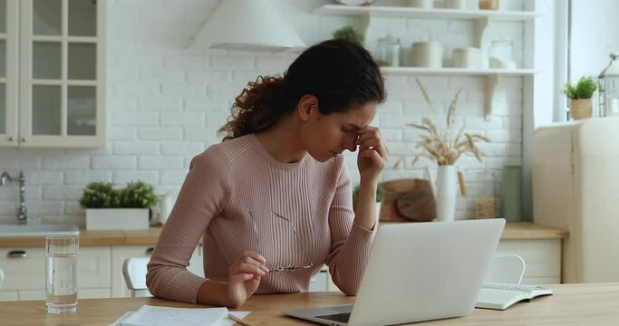 Young businesswoman taking off glasses massaging nose bridge, relaxing eyes, making break while working on computer at home. Busy female freelancer suffering from eyes strain due to laptop overwork.