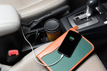 A businessman cell phone on the passenger seat and plugged into the cars charging port with coffee...
