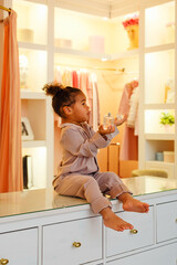 Baby cosmetics, cute little African American girl in the bedroom. Little cute girl doing makeup in the dressing room. A cute little girl in her mother's room.