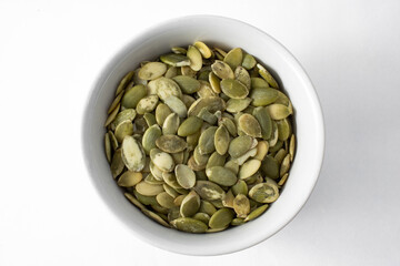 Top view of peeled and roasted pumpkin seeds, in bowl and isolated on white background