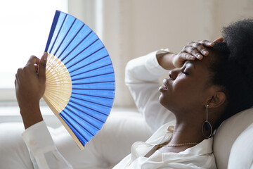 Tired Afro business woman suffering from heatstroke or hot summer flat without air-conditioner,...