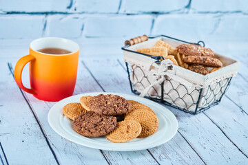 Assorted biscuits in plate and basket and a cup on blue table
