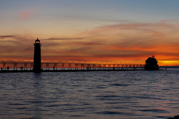 Fototapeta premium Grand Haven Lighthouse Michigan on Lake Michigan at sunset during the winter with beautiful colors and the structures and people silhouetted. Hot from North Pier.