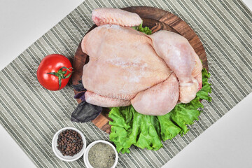 Raw whole chicken on wooden plate with lettuce, tomato and spices