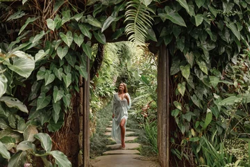 Fotobehang Young woman walking in tropical garden in long summer dress, greenery and palm trees around, enjoying nature © Yevhenii