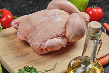 Raw whole chicken on wooden board with oil and tomatoes