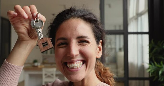 Head shot close up overjoyed young woman recording selfie video, showing keys from new adobe apartment. Happy millennial female homeowner feeling excited of purchasing house, real estate concept.