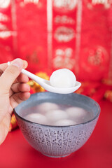 A bowl of dumplings or Yuanxiao on a festive red background with a spoon