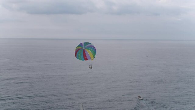 A panning view of people parasailing over a beautiful calm ocean on a cloudy day